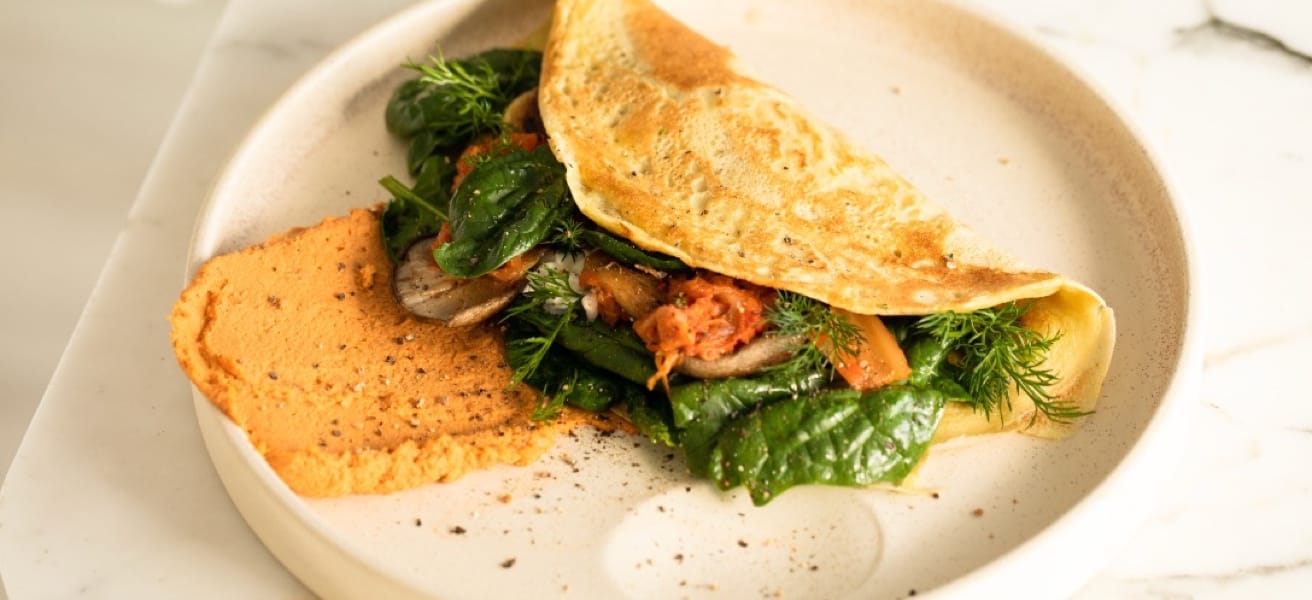 A freshly made folded omelette, with fresh greens and a dressing on the side